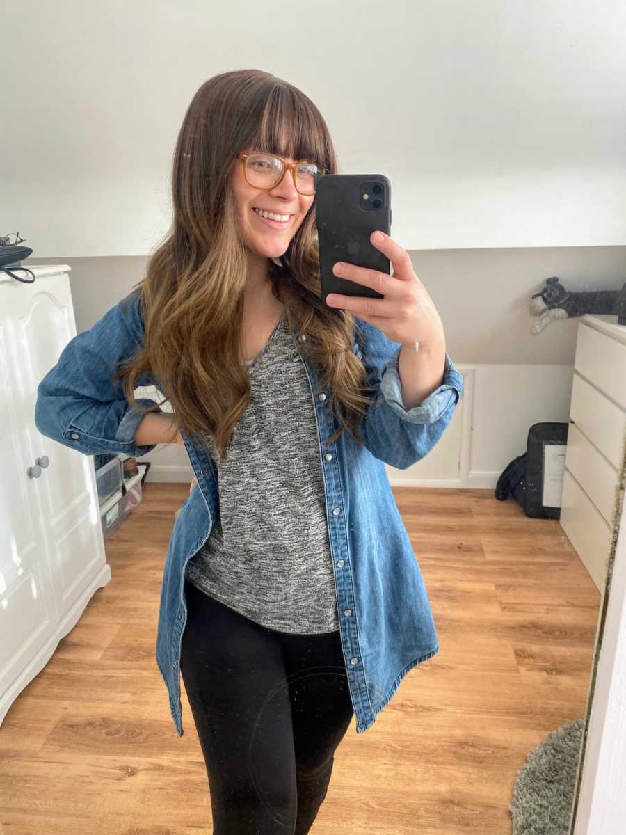 Woman wearing jean jacket taking smiling mirror selfie