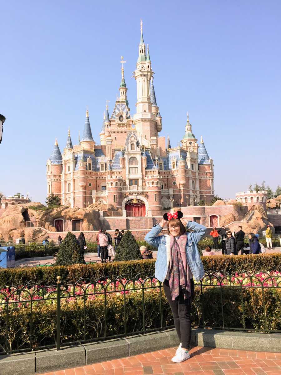 Woman at Disney wearing Mickey Mouse ears posing in front of castle