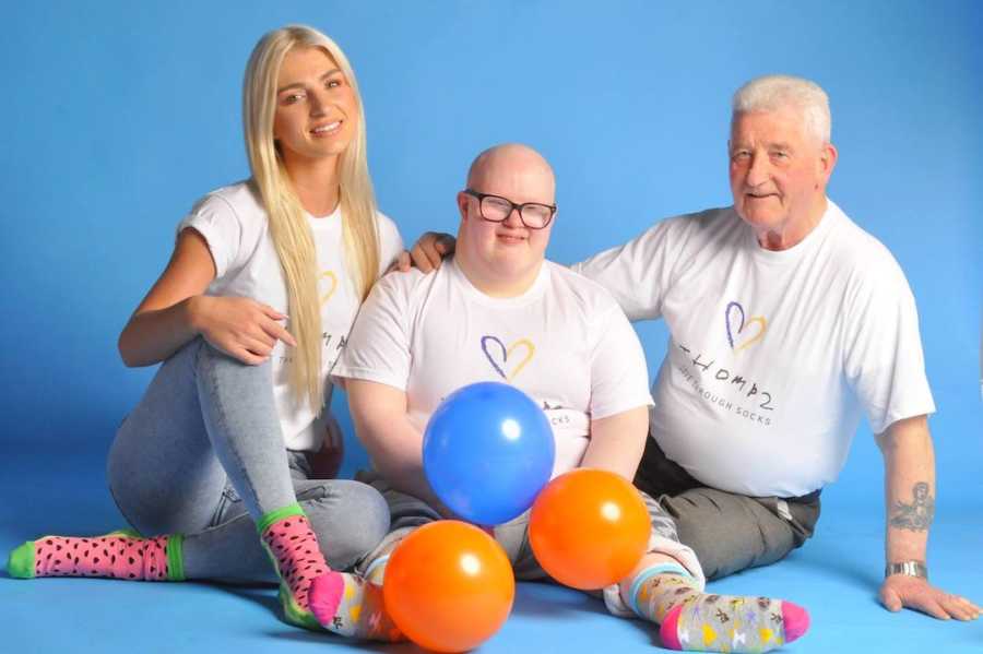 Three people sitting on the floor in front of blue background with balloons