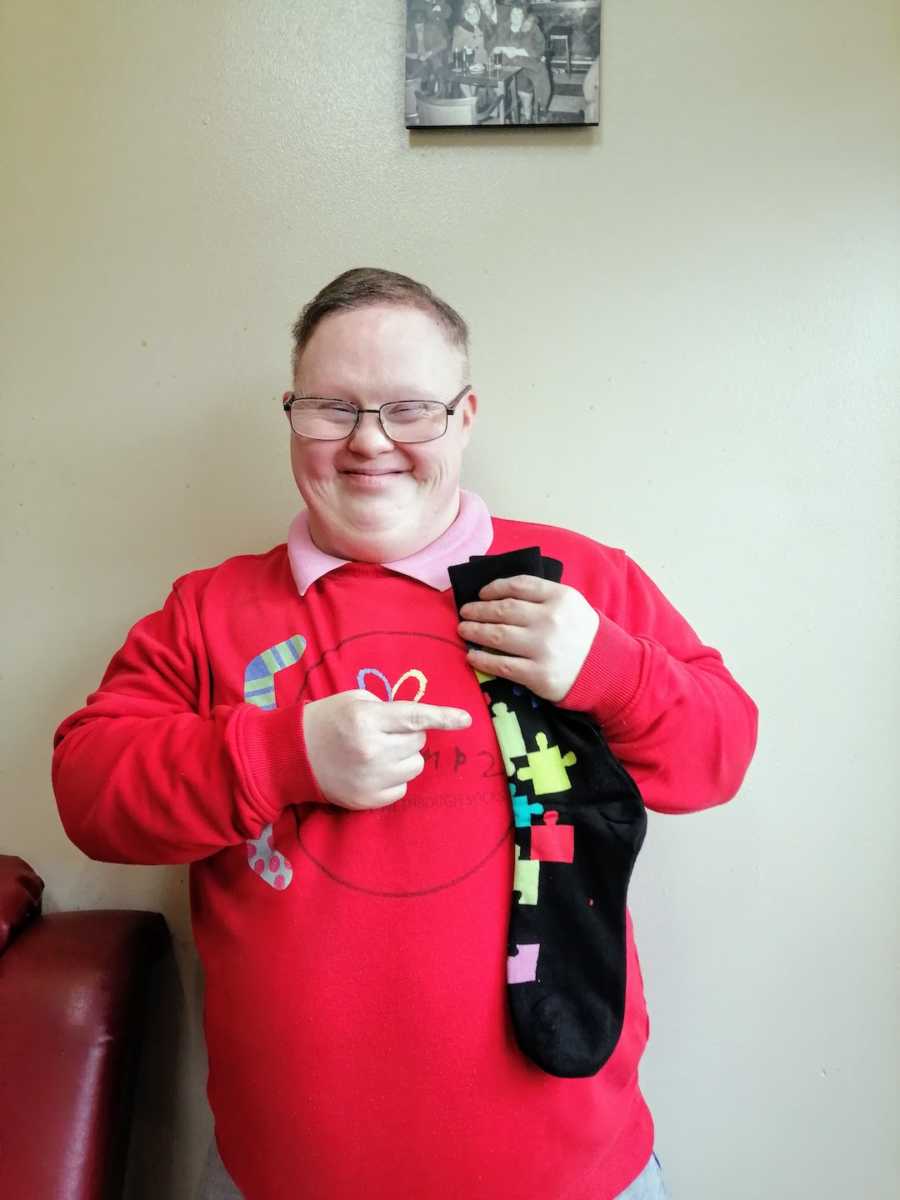 Man wearing red sweater holding up socks with puzzle pieces