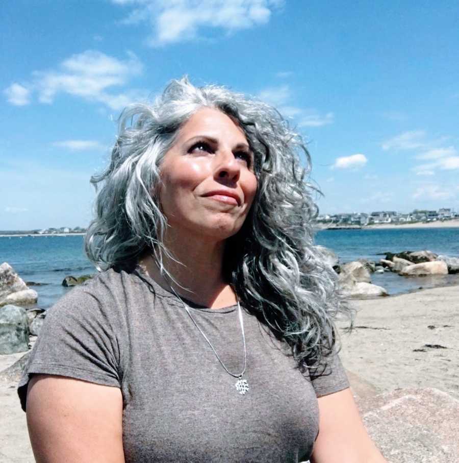 Woman with gray hair looking into sky standing on the beach