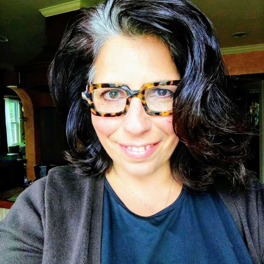 Woman with black hair and gray roots taking smiling selfie