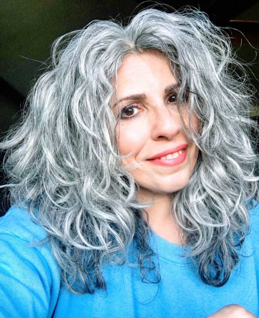 Woman with gray hair wearing blue shirt taking smiling selfie