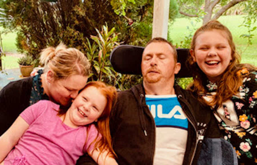 Family of four with father in wheelchair all smiling and laughing