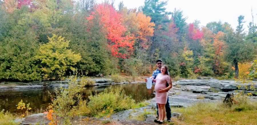 Expecting parents take a pregnancy announcement photo with a beautiful outdoor scene around them