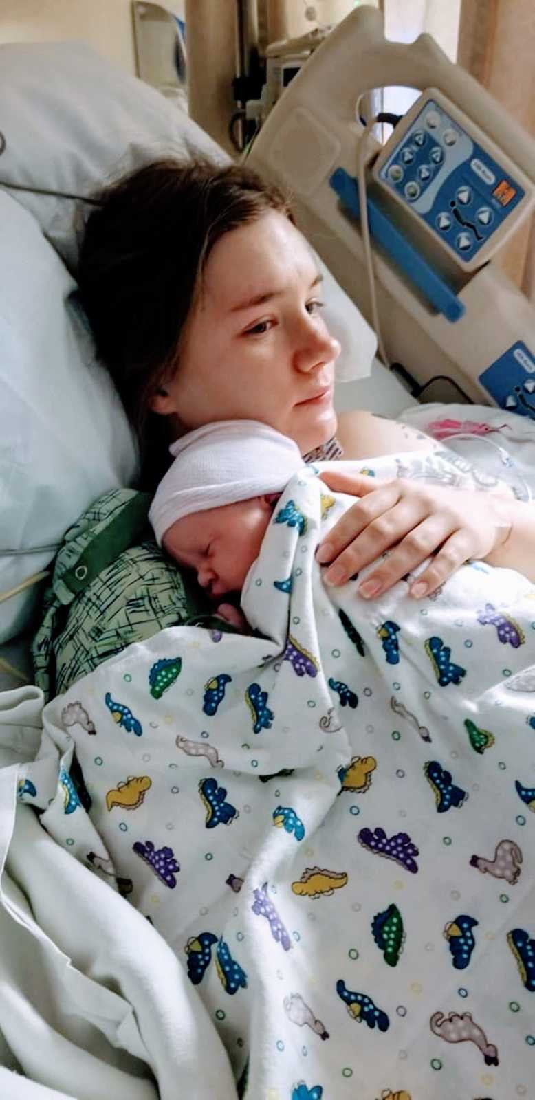 Mom holds her newborn daughter wrapped up in a dinosaur blanket in the hospital after giving birth