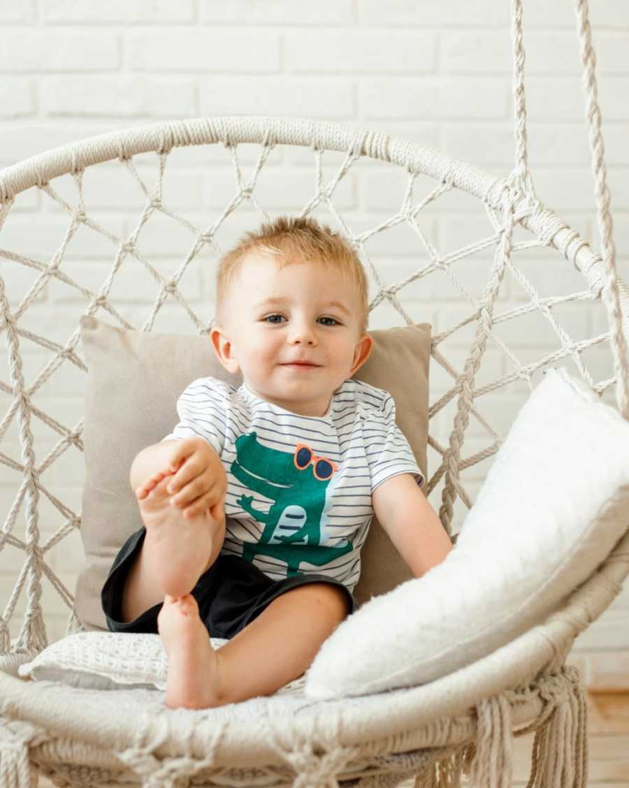 Little boy with an alligator shirt on smiles for a photo while sitting in a white swing chair