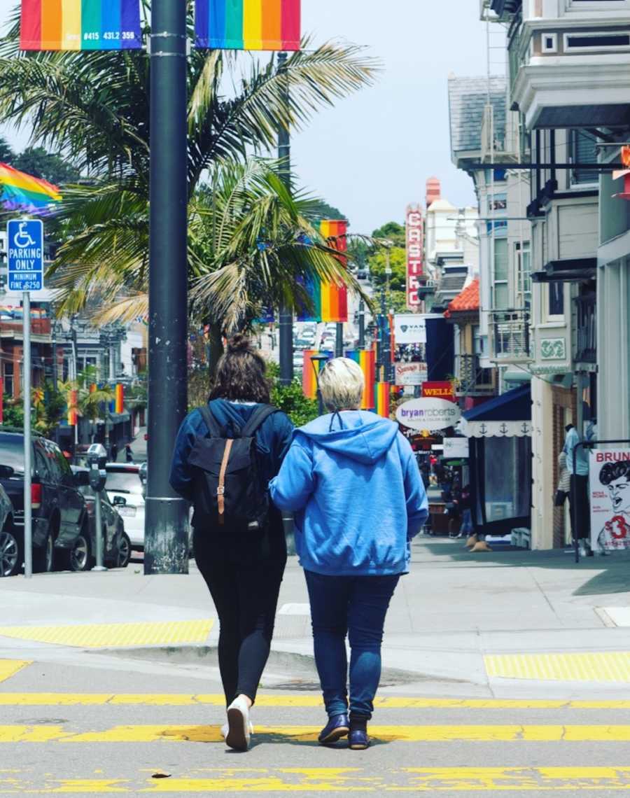 two women walking in street with rainbow flag