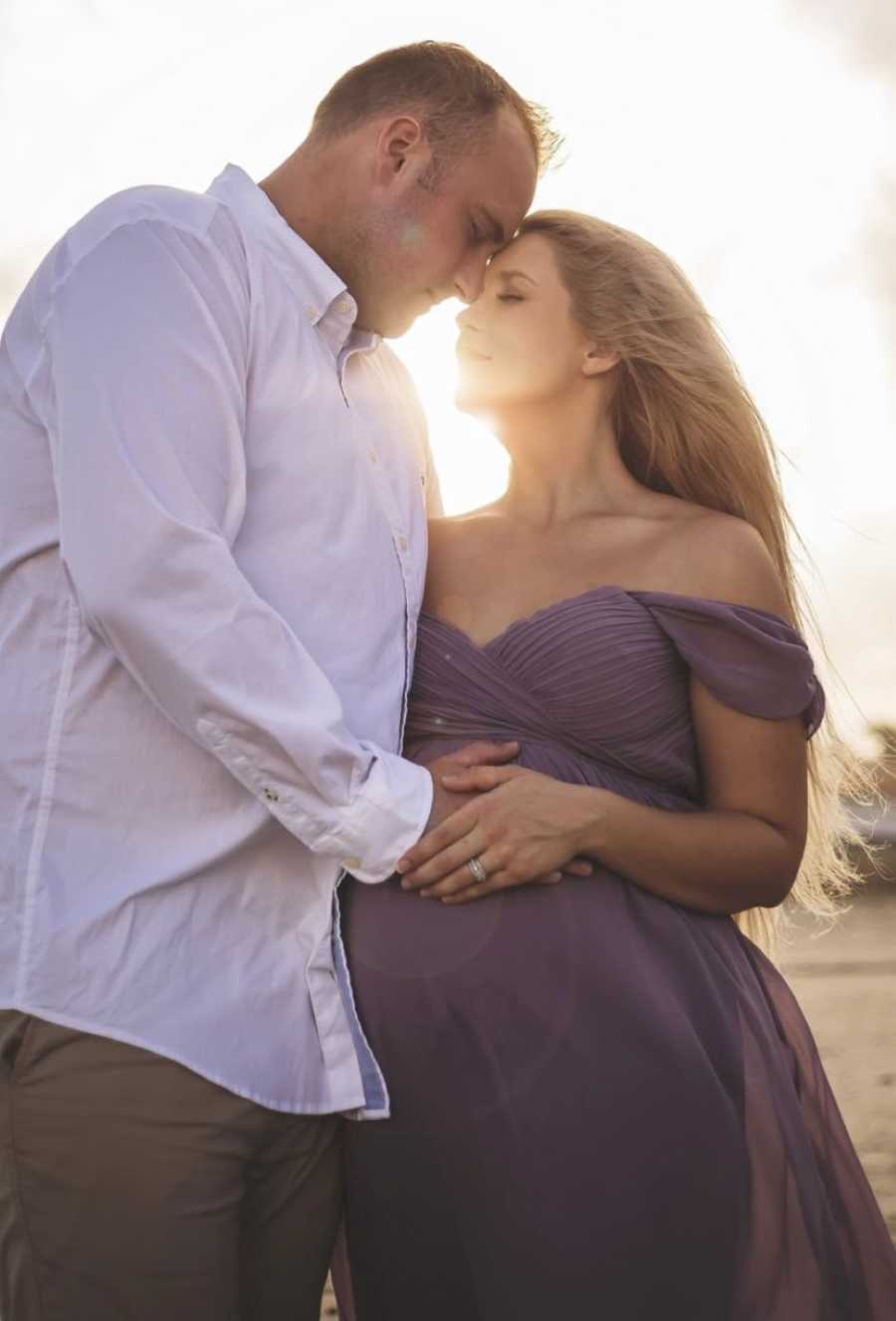 Couple expecting their second daughter together take beautiful maternity photo in matching purple outfits on the beach