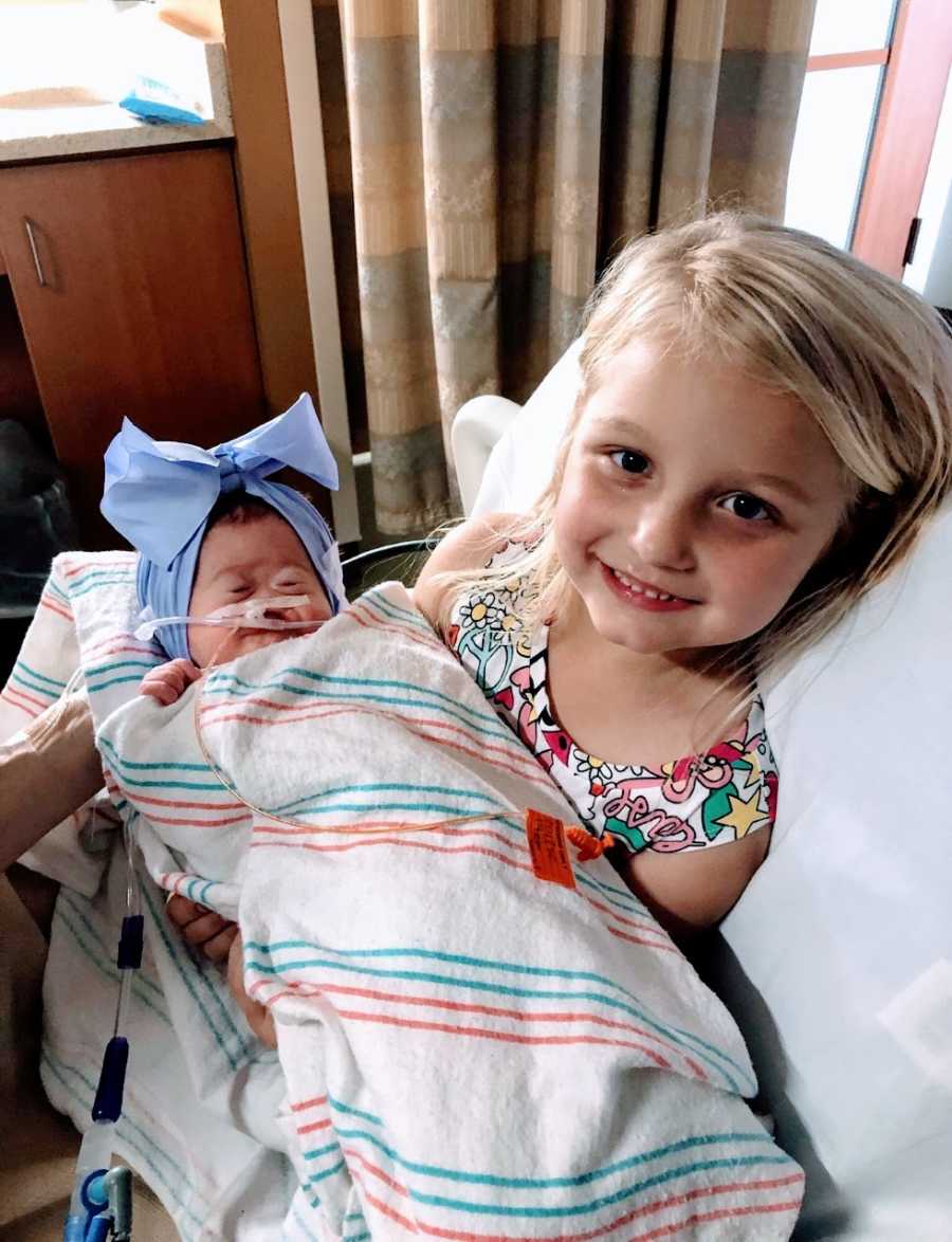 Young girl holds her newborn baby sister with rare Alobar Holoprosencephaly in the hospital