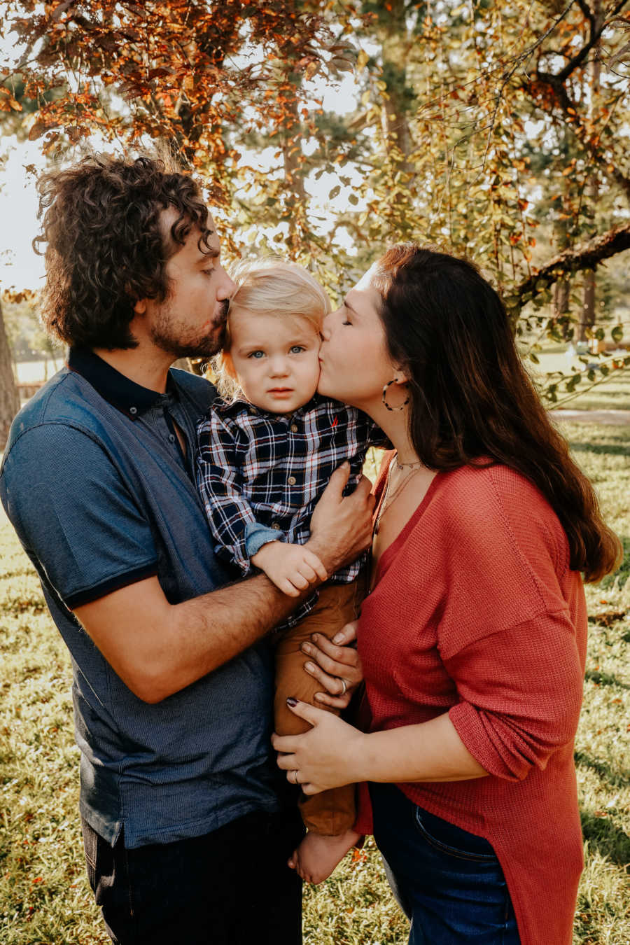 Parents hold their son between them and kiss his cheeks