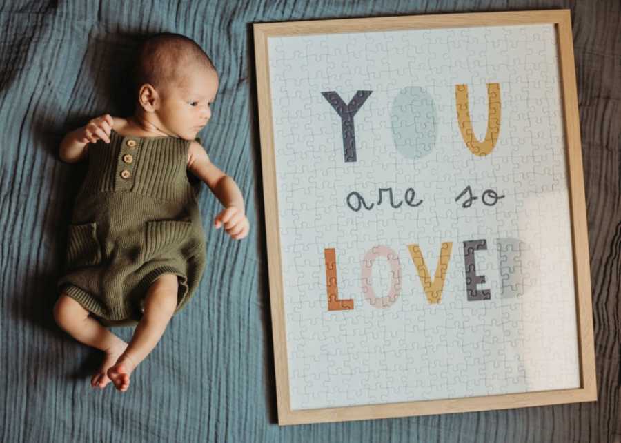 Couple take photo of their newborn adopted son next to a puzzle that says 'You are so loved'