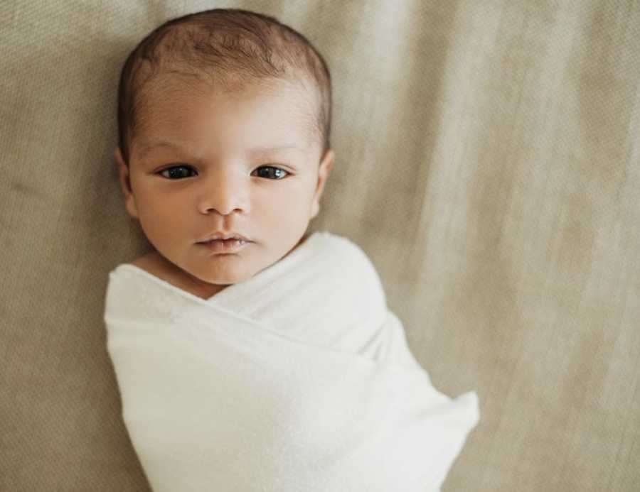 Adoptive parents take photo of their newborn adopted son swaddled in a white blanket