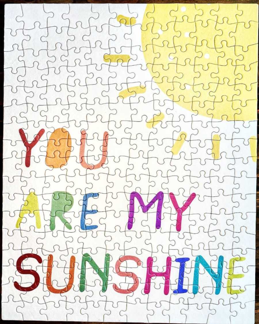 Couple fundraising money for their adoption sell puzzle pieces, the completed puzzle says 'You are my sunshine' with a sun on it