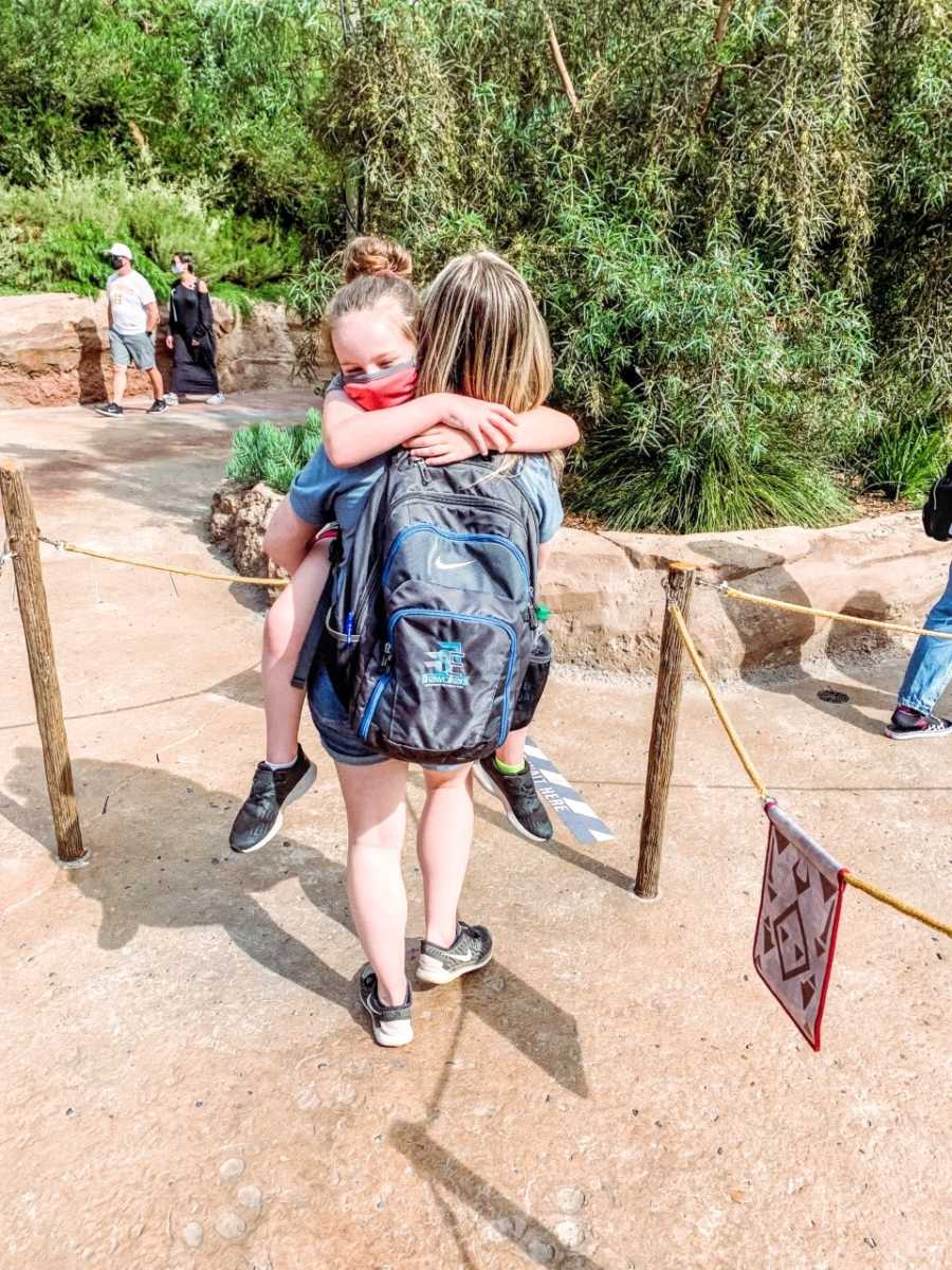 Girl mom holds tired daughter while in line for a ride at Disneyland