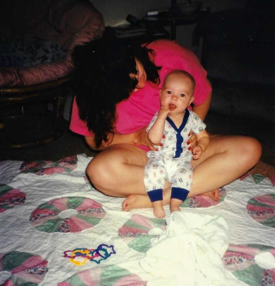 Mom looks down at newborn son while they play together on the floor