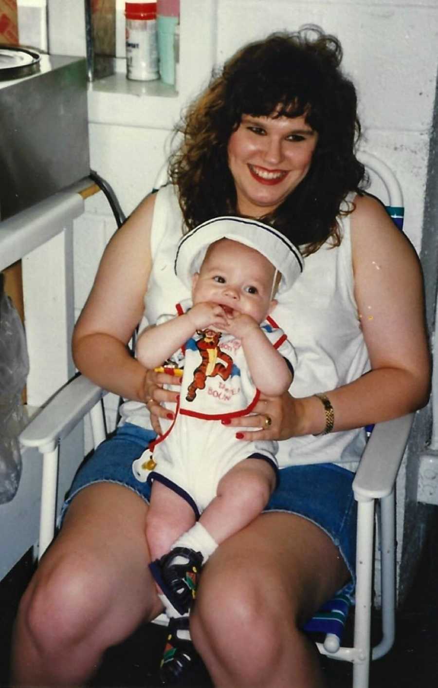 Mom smiles while holding her first son in a hat and onesie