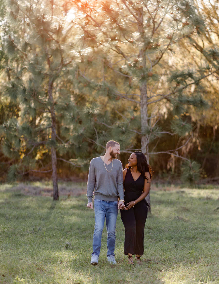 Young interracial couple walk hand-in-hand while smiling at each other, full of love