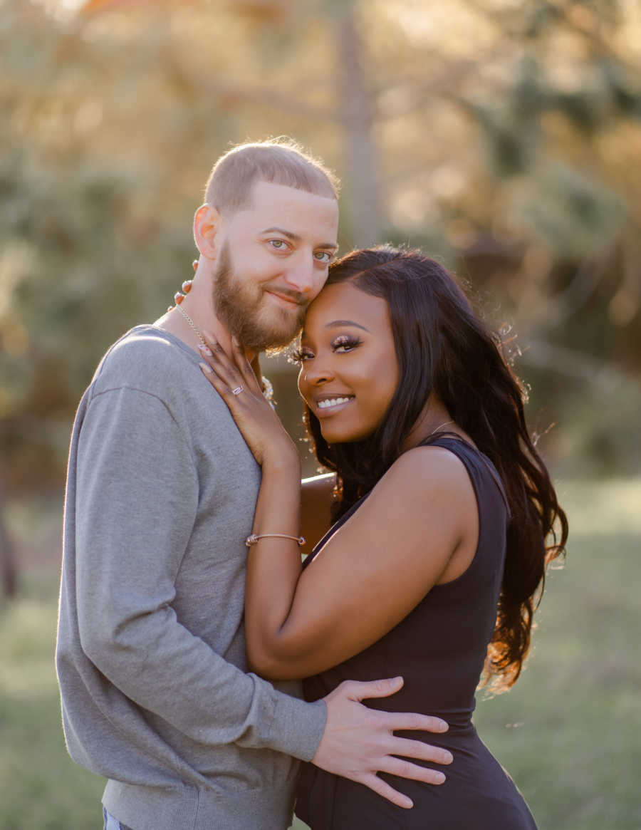 Young interracial couple smile at the camera while embracing each other during a photoshoot