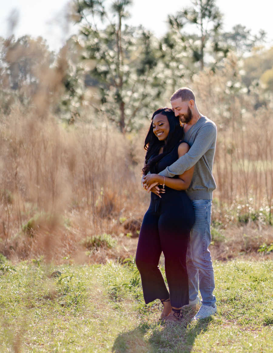 Young interracial married couple embrace in a field during a photoshoot