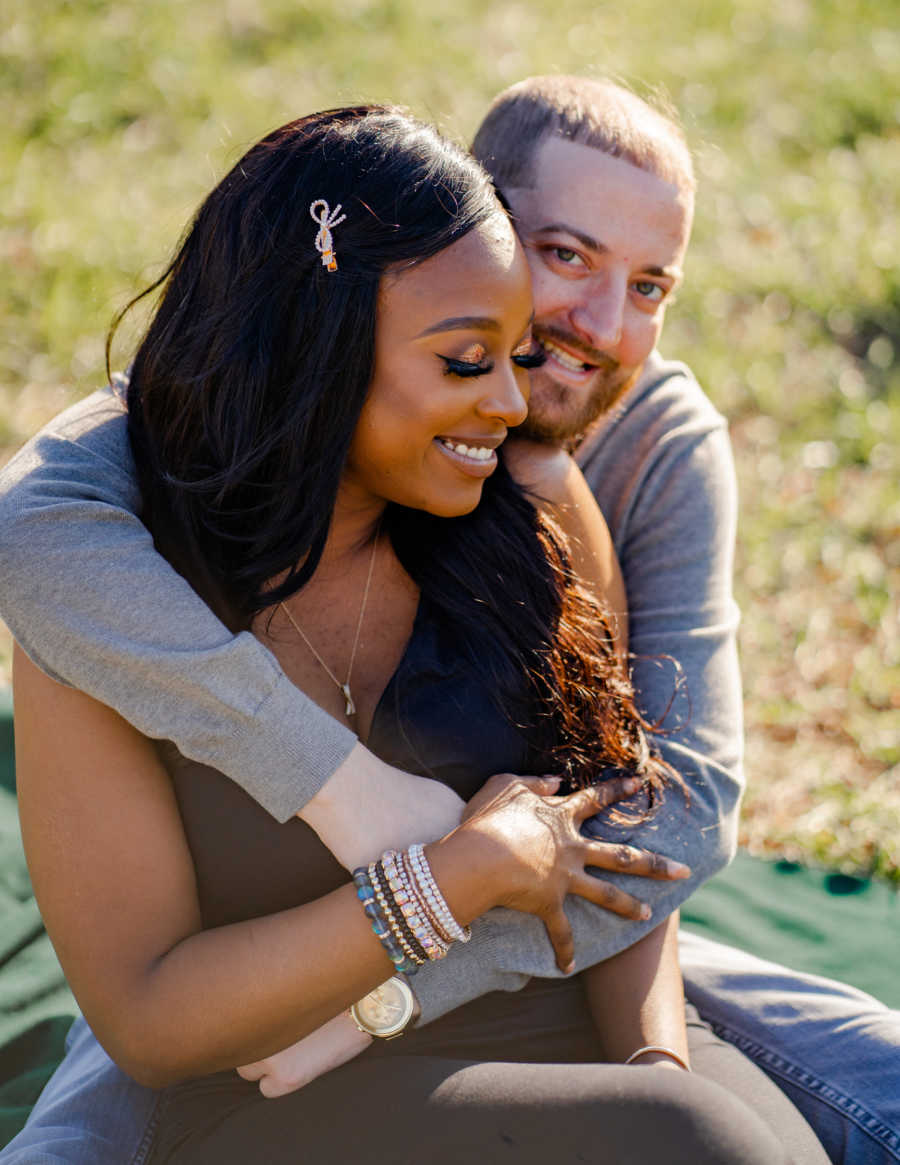 Young interracial couple embrace while sitting down on a green blanket