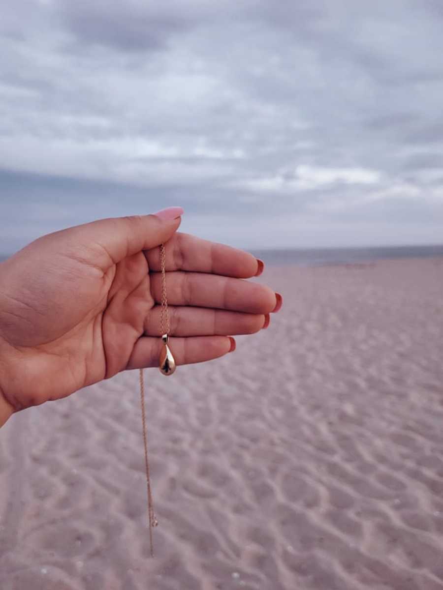 hand holding necklace in front of beach