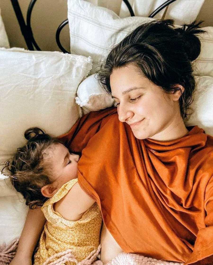 Mom smiles down at her baby girl while they cuddle together in bed during an afternoon nap