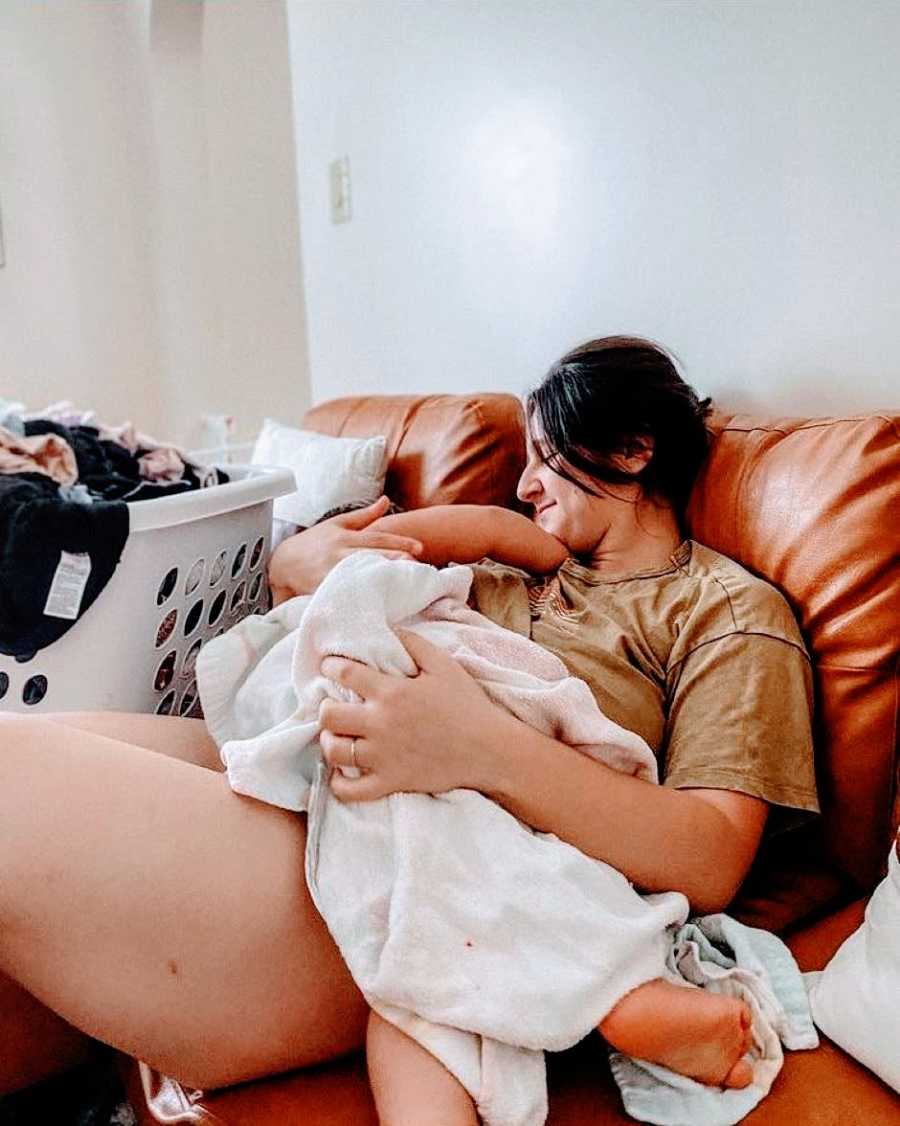 Mom of 2 breastfeeds toddler while sitting on the couch next to laundry