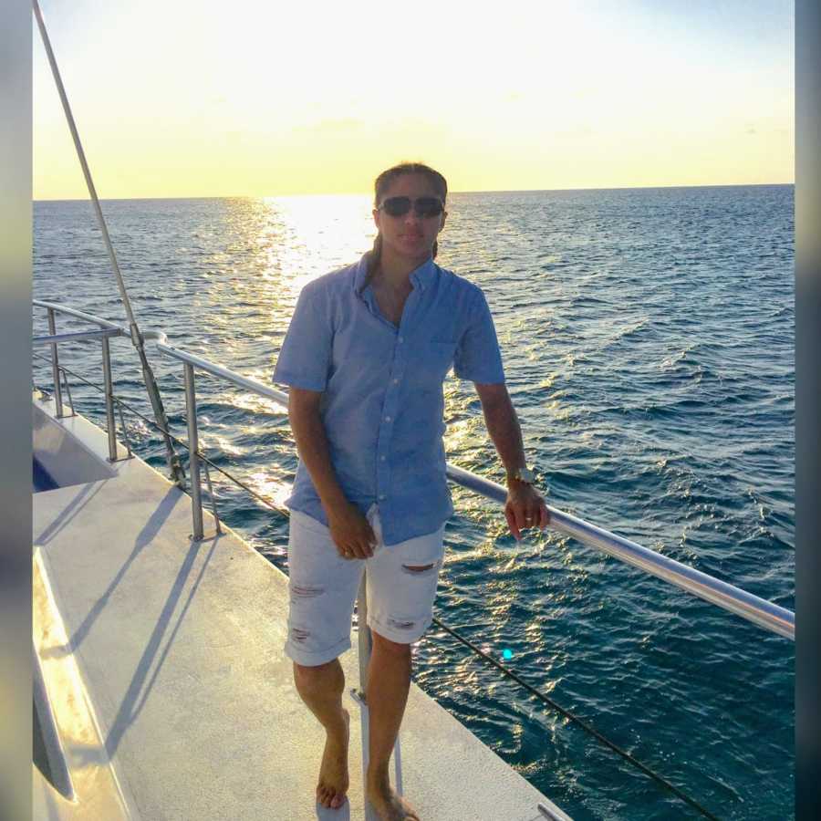 Lesbian woman takes a serious photo while standing on a boat, watching the sunset