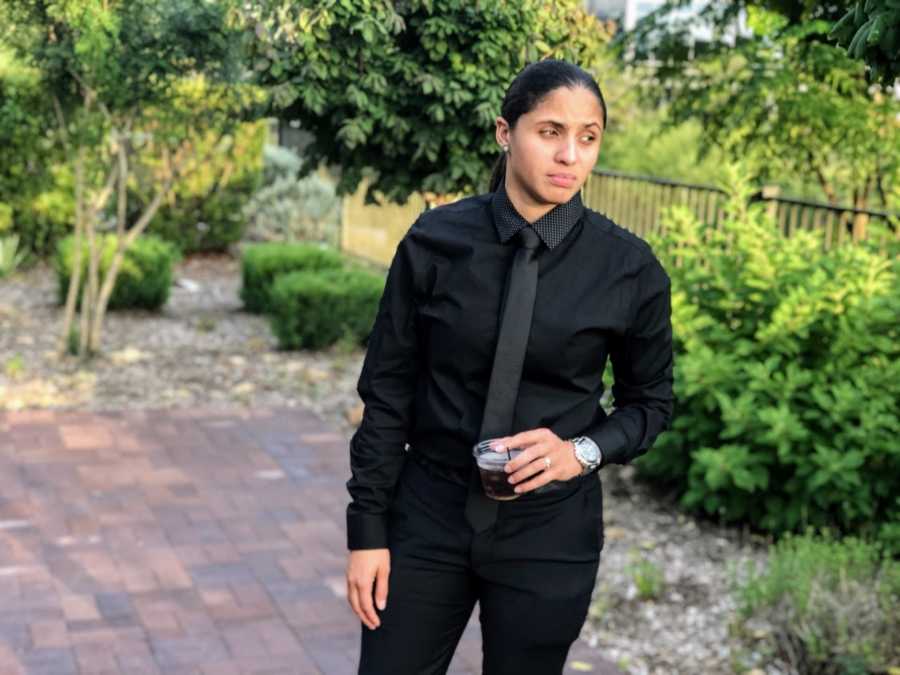 Woman looks serious in photo, wearing all-black suit and holding a drink