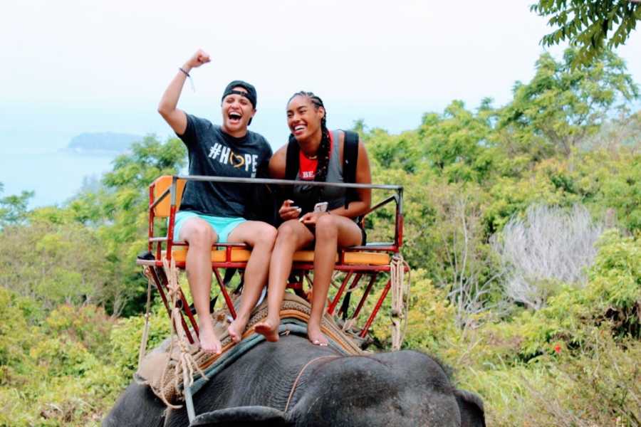 Lesbian woman cheers while riding an elephant with her wife