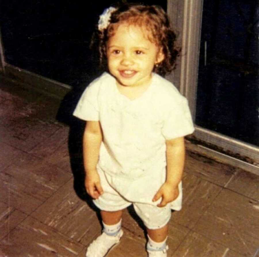 Little girl stands and poses for a photo in an all-white outfit with a white bow in her hair