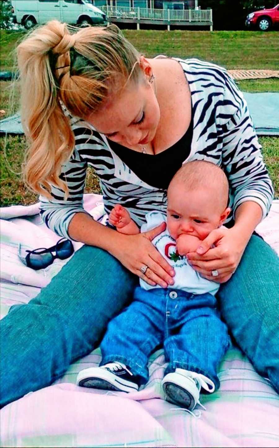 Young mom spends time with her infant son outside on a blanket while wearing a zebra print shirt