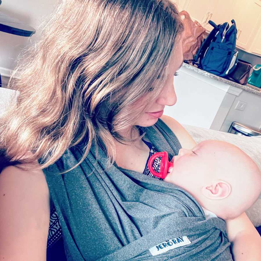 First time mom looks down at her swaddled newborn son as he sleeps