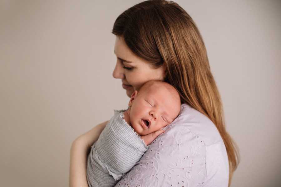 Mom embraces her sleeping newborn son during postpartum photoshoot