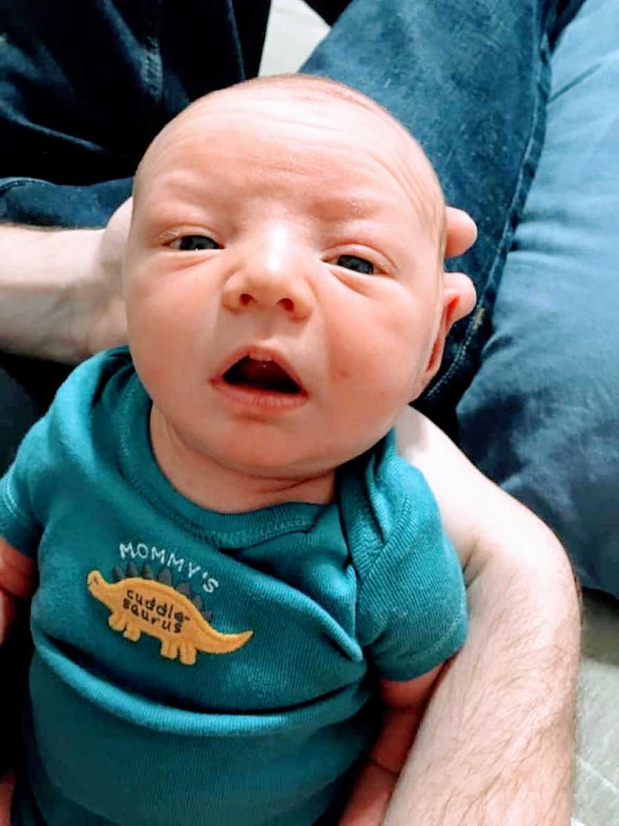 Mom takes a photo of her newborn son wearing a onesie that reads "Mommy's cuddle-saurus" with a dinosaur on it