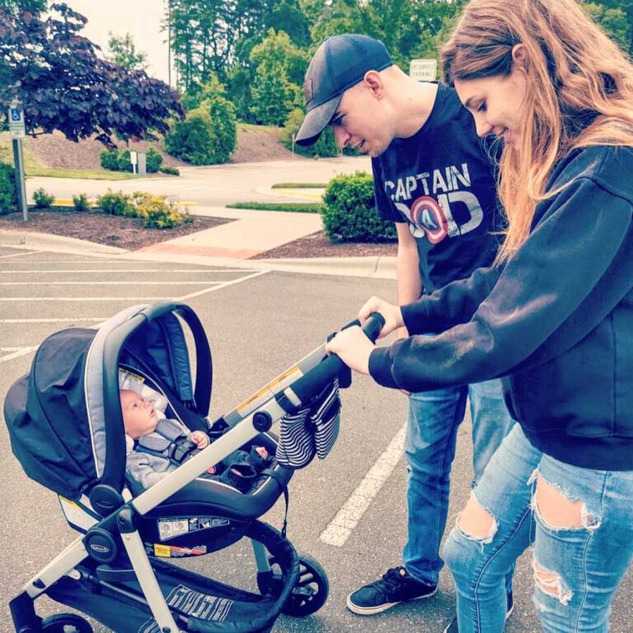 First time parents stare at their newborn son while he lays in his stroller during a family walk