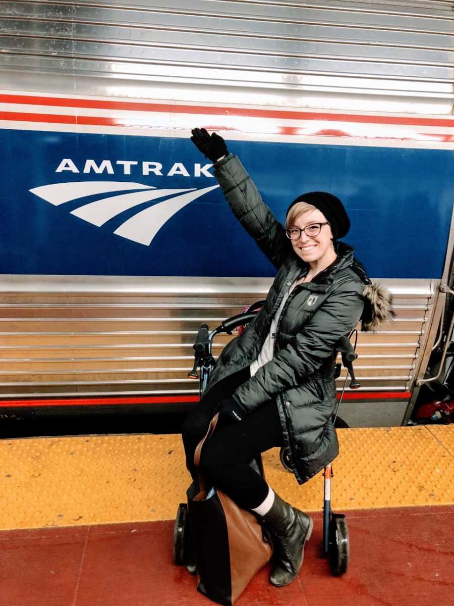 College student sits on her walker and takes a photo in front of an Amtrack train