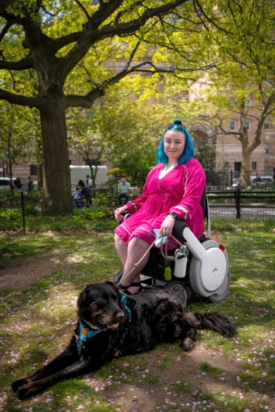 Woman in wheelchair with blue hair takes a photo with her service dog in New York park