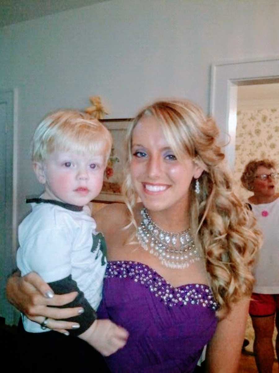 Teen girl holds her baby brother while getting ready for Homecoming in purple dress