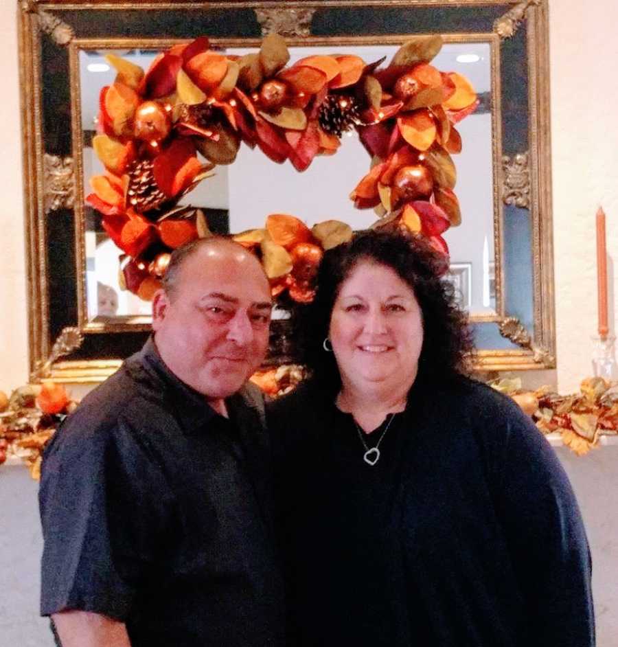 Married couple take photo together at Thanksgiving dinner with fall-themed decorations behind them