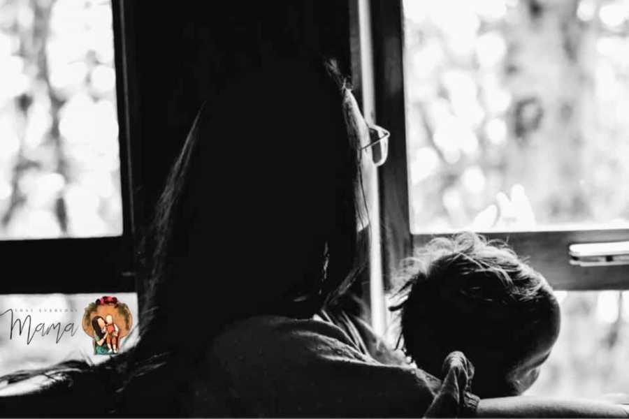 Woman stares out the window while holding her child and reflecting on overcoming her childhood trauma