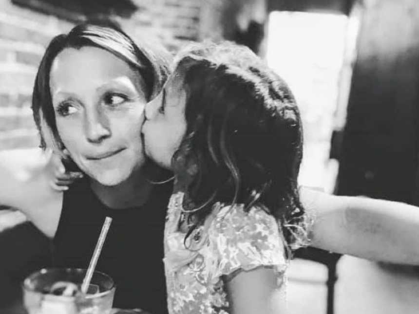 Mom takes a photo with her daughter while she kisses her on the cheek