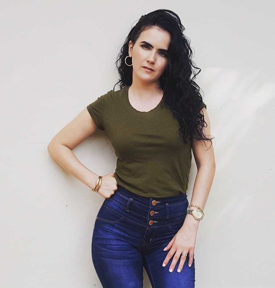 woman confidently smiling in olive top and jeans, hand on hip