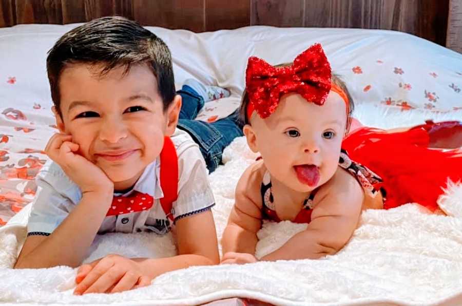 A little boy and his baby sister lying on a bed