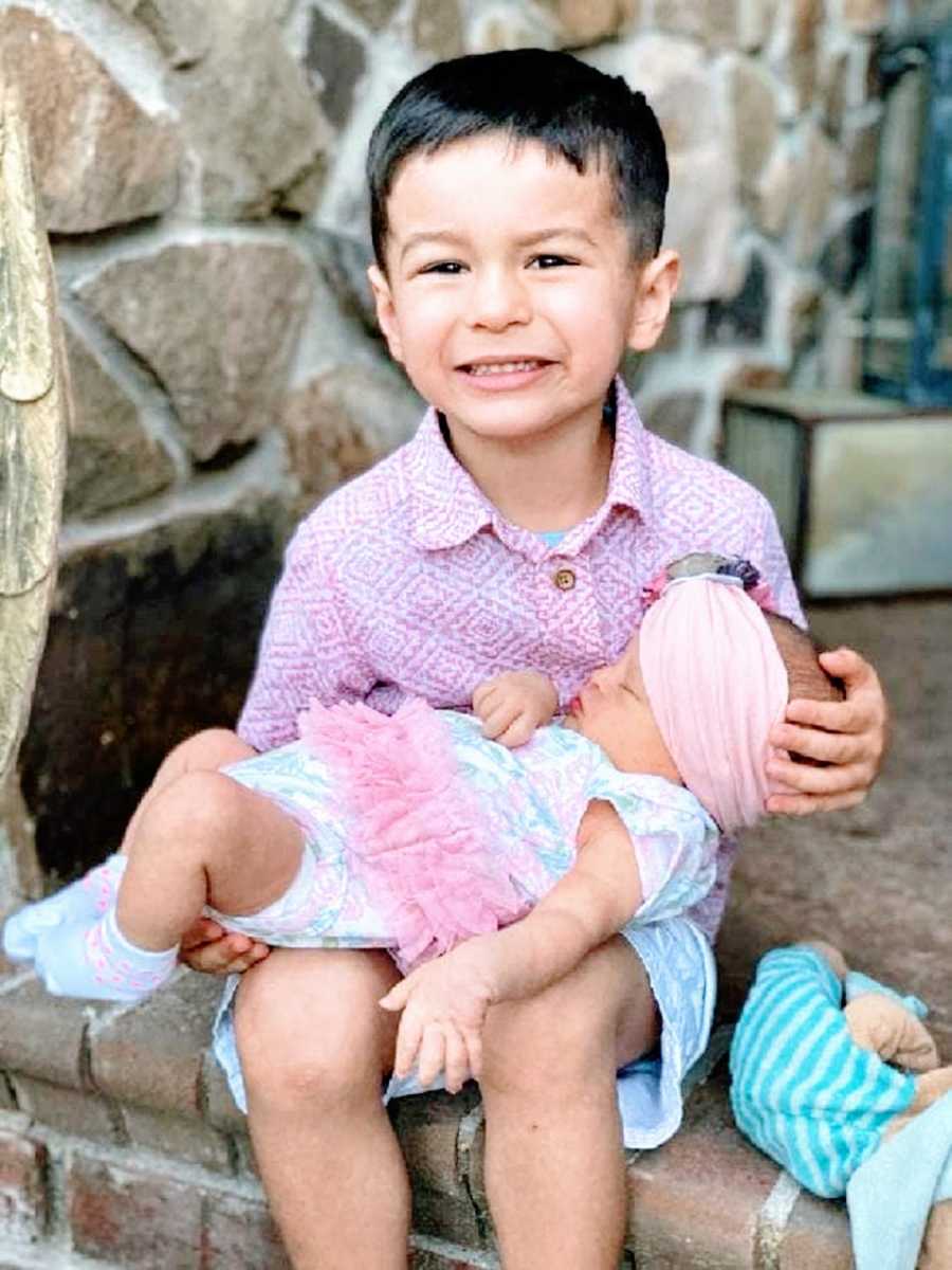 A little boy holds his baby sister on his lap