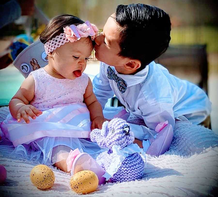 A little boy kisses his baby sister on the forehead