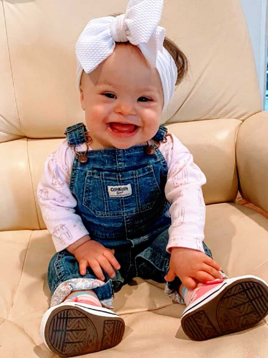 A baby girl wearing overalls and a bow on her head