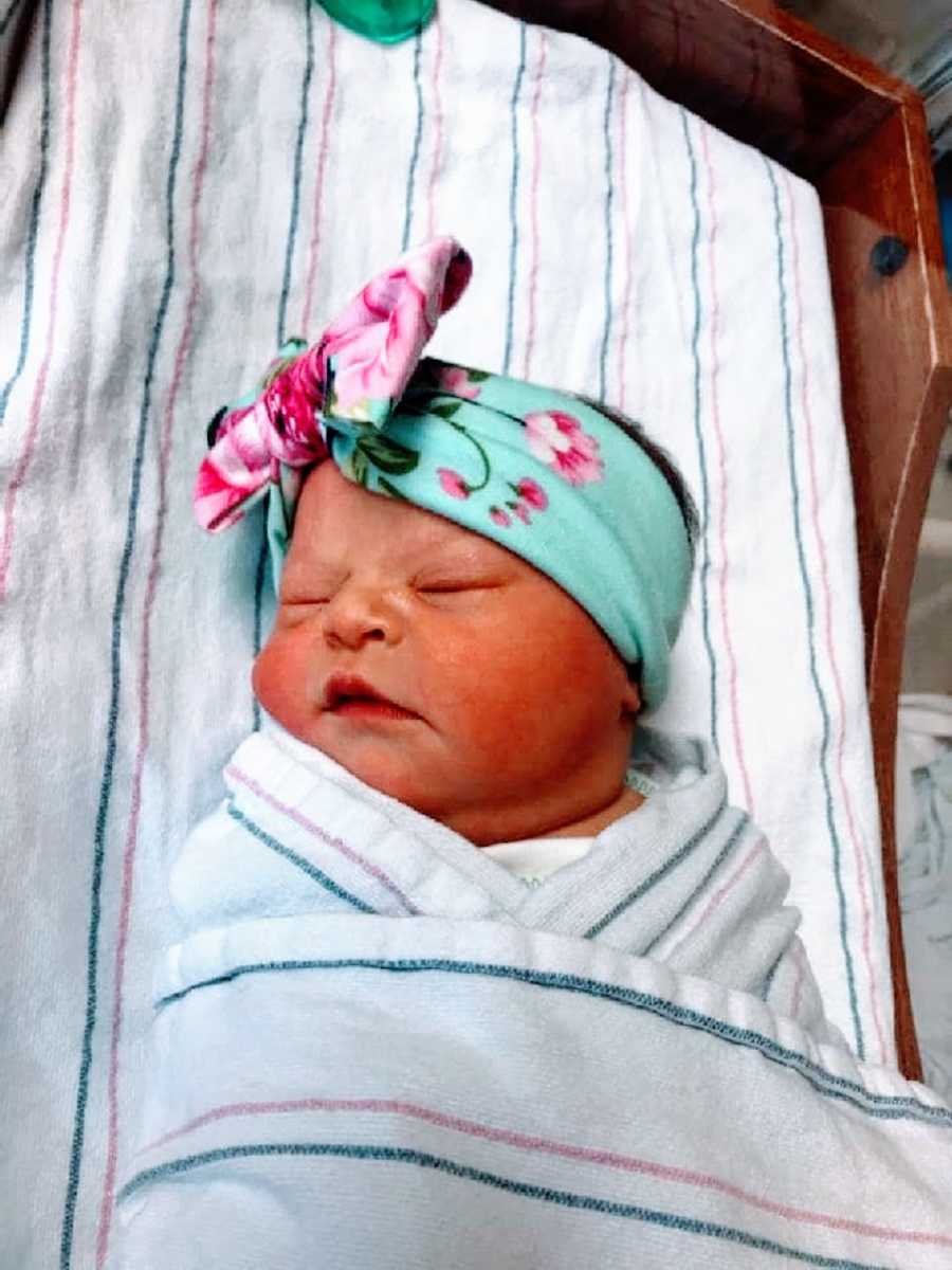 A newborn baby girl swaddled and wearing a bow on her head