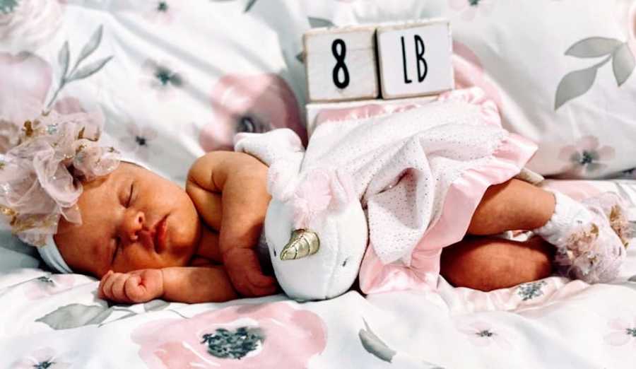 A newborn baby girl lying next to a marker that says 8lb